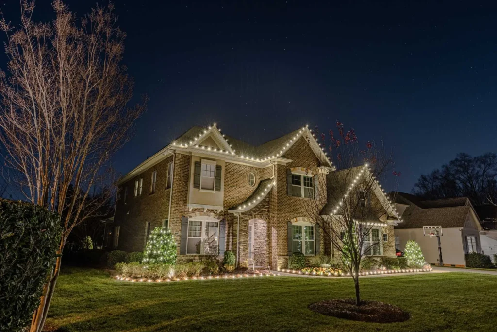Two-story residence with warm white roofline Christmas lights and front-yard lighting