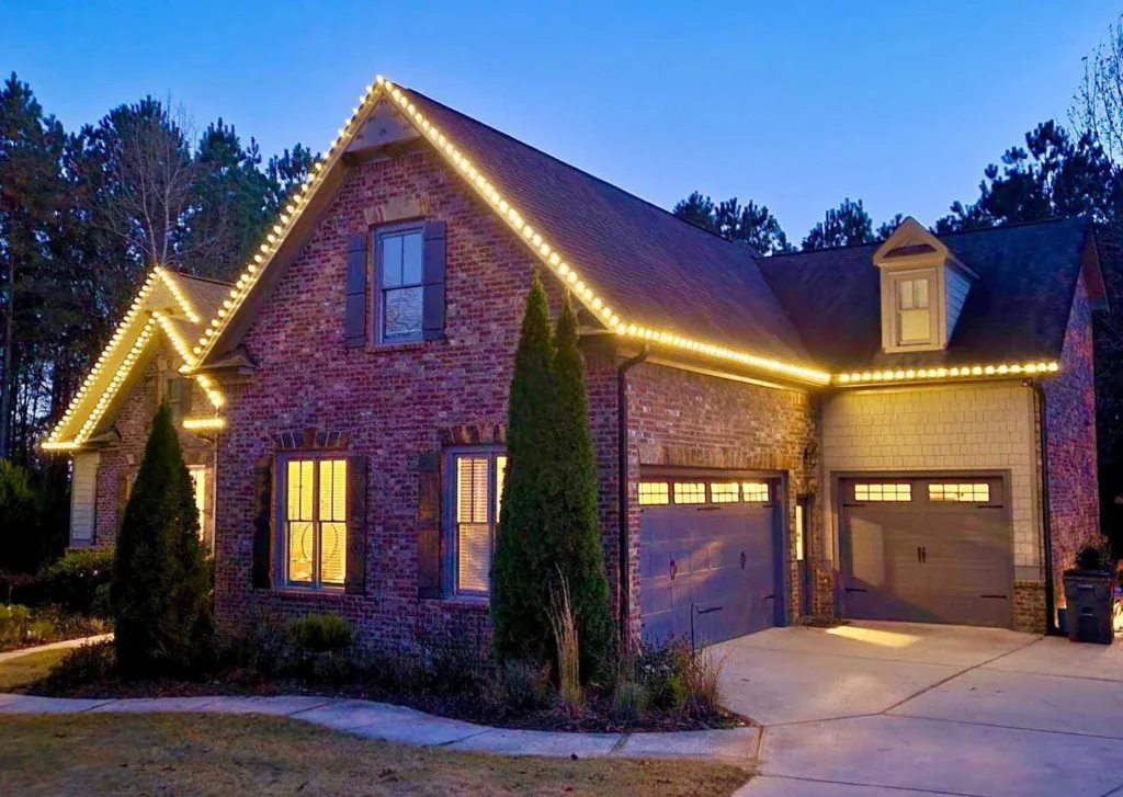 Red-brick home with warm white Christmas lights tracing the roofline and garage