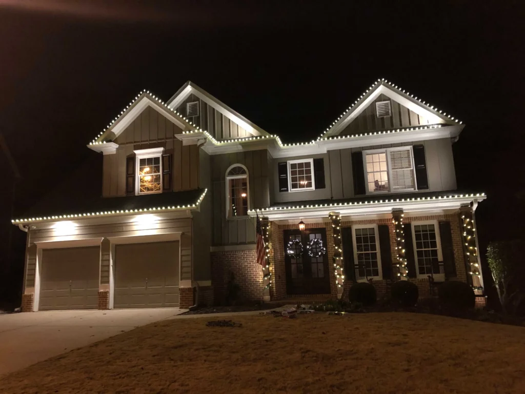 Large two-story home with warm white Christmas lights along the roofline, windows, columns, and entry