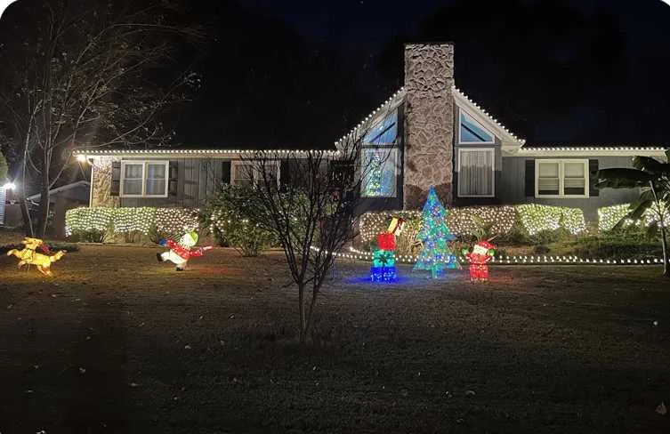 Home with warm white roofline lights and colorful Christmas yard decorations at night