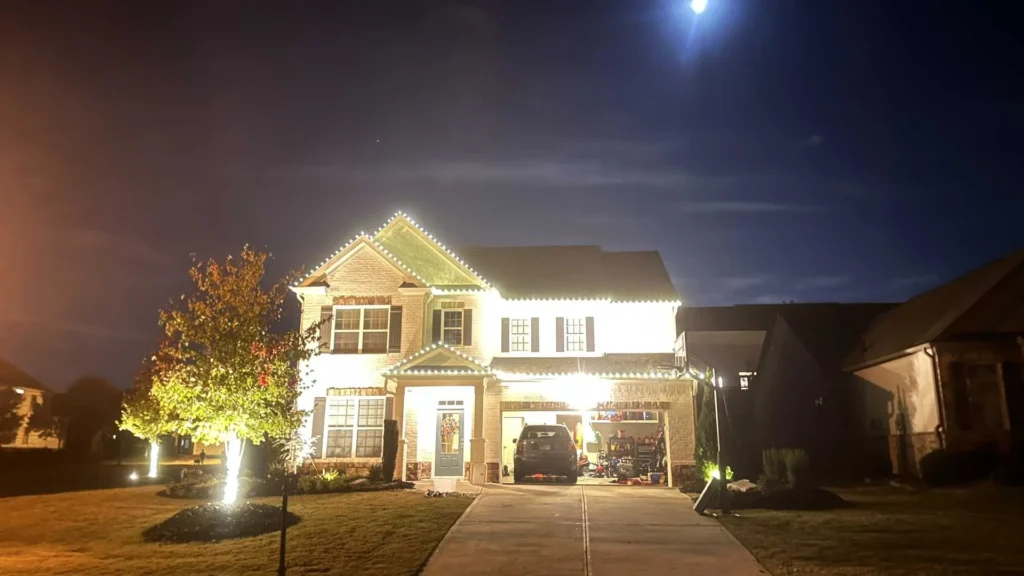 Two-story home brightly outlined with warm white Christmas lights across the roofline and garage