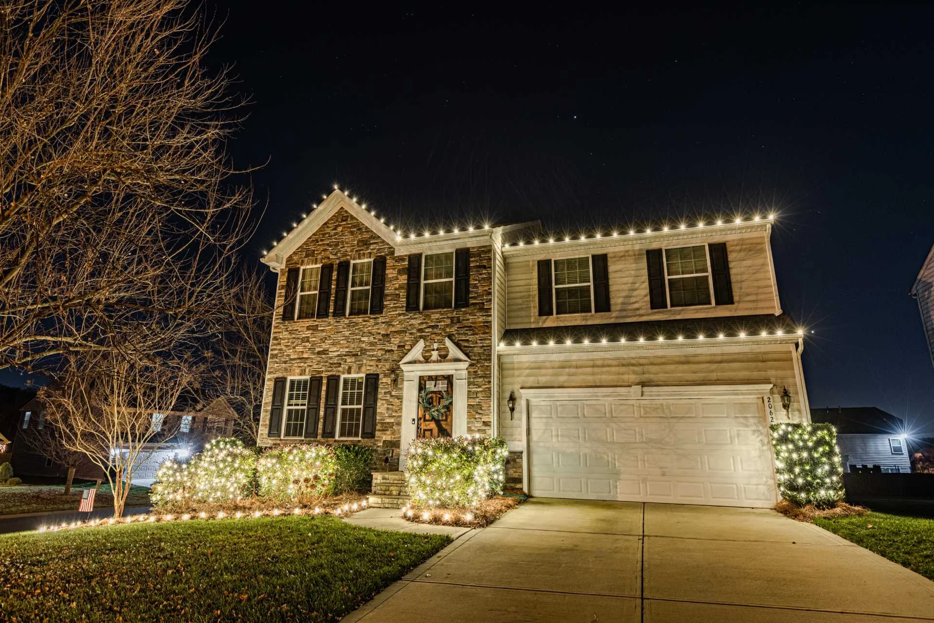 Two-story home with warm white Christmas roofline lights and illuminated front landscaping