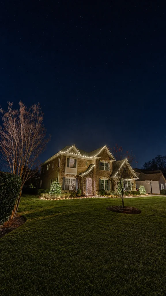 Vertical view of a home with warm white roofline Christmas lights and illuminated landscaping