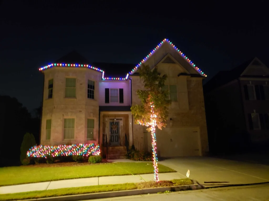 Colorful Christmas lights outlining a two-story home roofline with a lit front-yard tree